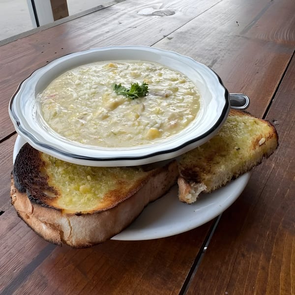 Creamy clam chowder in a white bowl with two slices of toasted garlic bread on a wooden table.