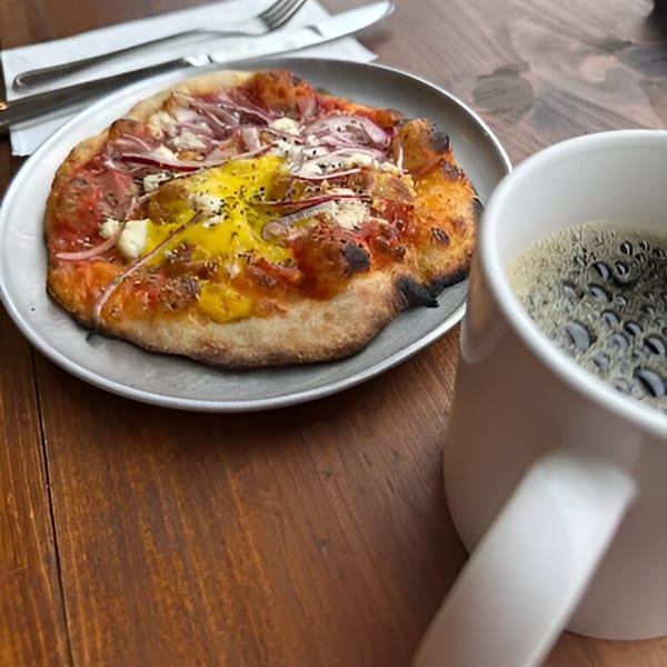 Cafe Enza's breakfast pizza with egg, bacon, and onions, served with a cup of coffee.
