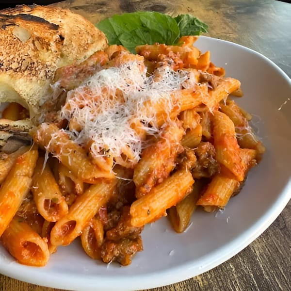 Cafe Enza's penne pasta with meat sauce, topped with parmesan cheese, basil, and toasted bread.
