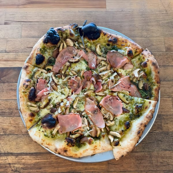Cafe Enza's pesto pizza with mushrooms and prosciutto on a metal tray.