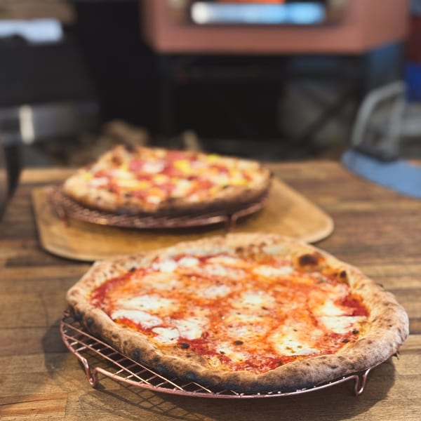 Two freshly baked pizzas, one Margherita and one pepperoni, on a wooden table at Cafe Enza.